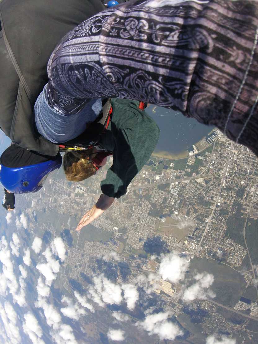 A photo of Lydia skydiving. There are clouds and land below. A photo of Lydia skydiving. There are clouds and land below.