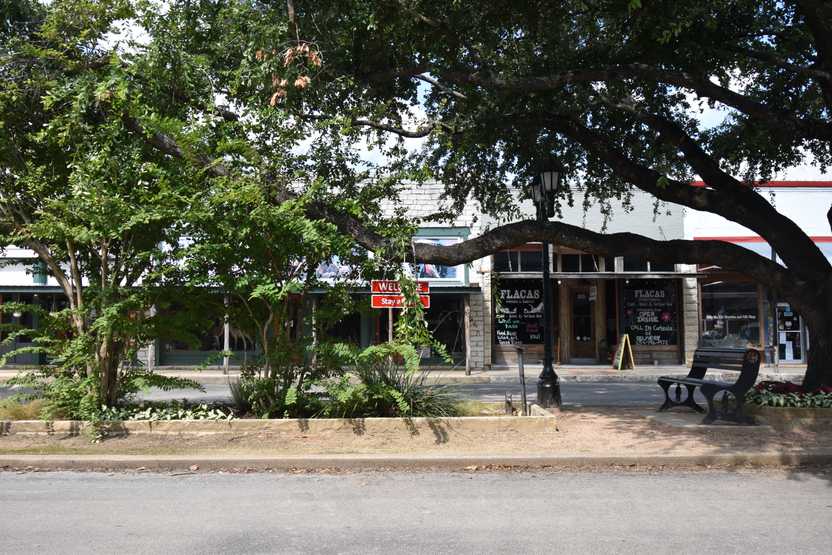 Looking across the street at some businesses in downtown Hico. The sidewalk is lined with trees.