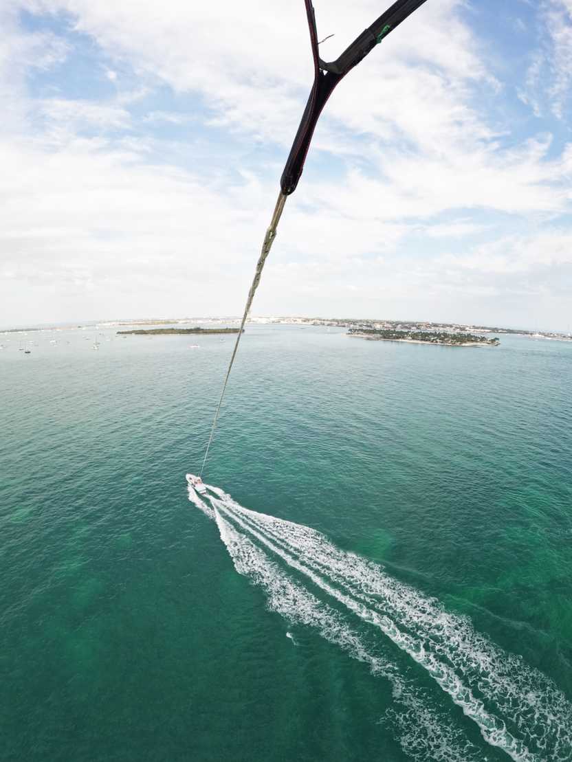 The view looking down at the ocean at the boat from parasailing in the sky
