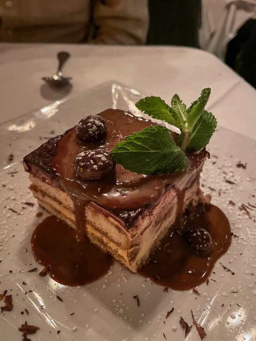 A tiramisu dessert from Mamma Maria. There is a green garnish on top and a chocolate sauce dripping from the top.