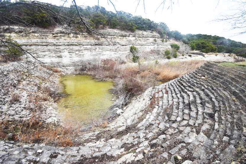 A spillway with many layers of stones layering down to a pool of water.