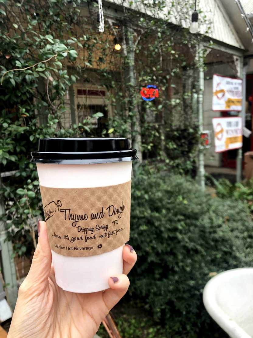 Holding up a to-go coffee mug that says "Rolling in Thyme and Dough" on the paper sleeve.
