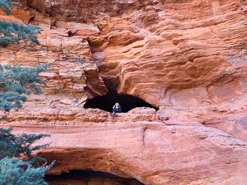 Lydia sitting inside a small cave that is up on a cliff face.