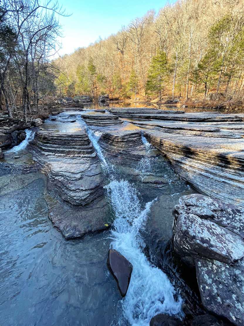 Three small waterfalls cascading down over layers of rocks.
