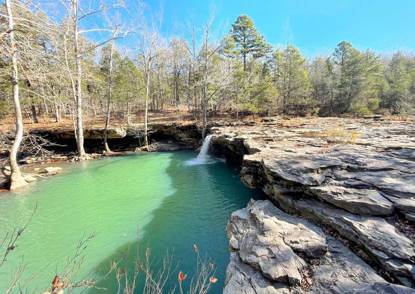 A small waterfall coming down over a rock face with a green pool of water.