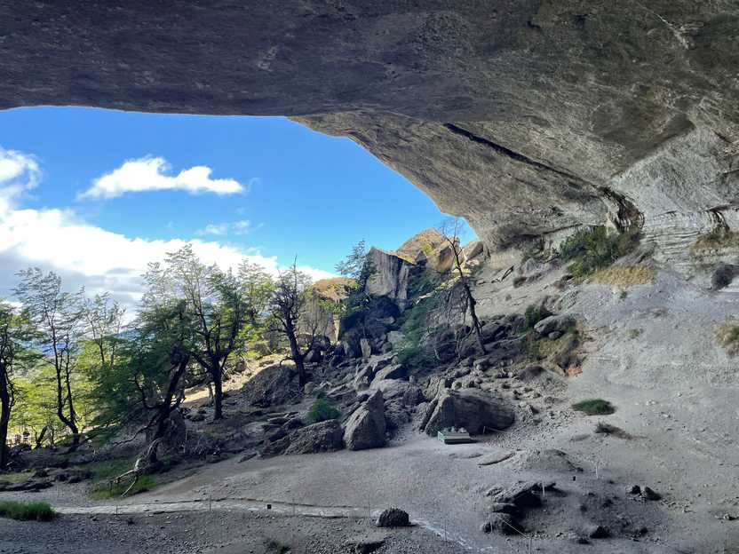 Looking out from the inside of a giant cave. There are some huge rocks and green trees outside of the cave.