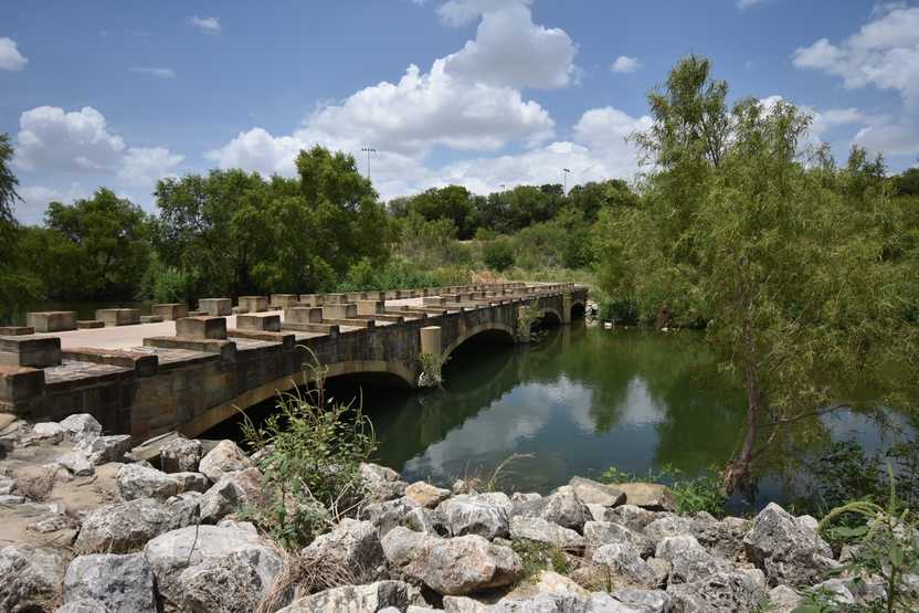 A view of the river with a road crossing over it and stones lining the side of the water.