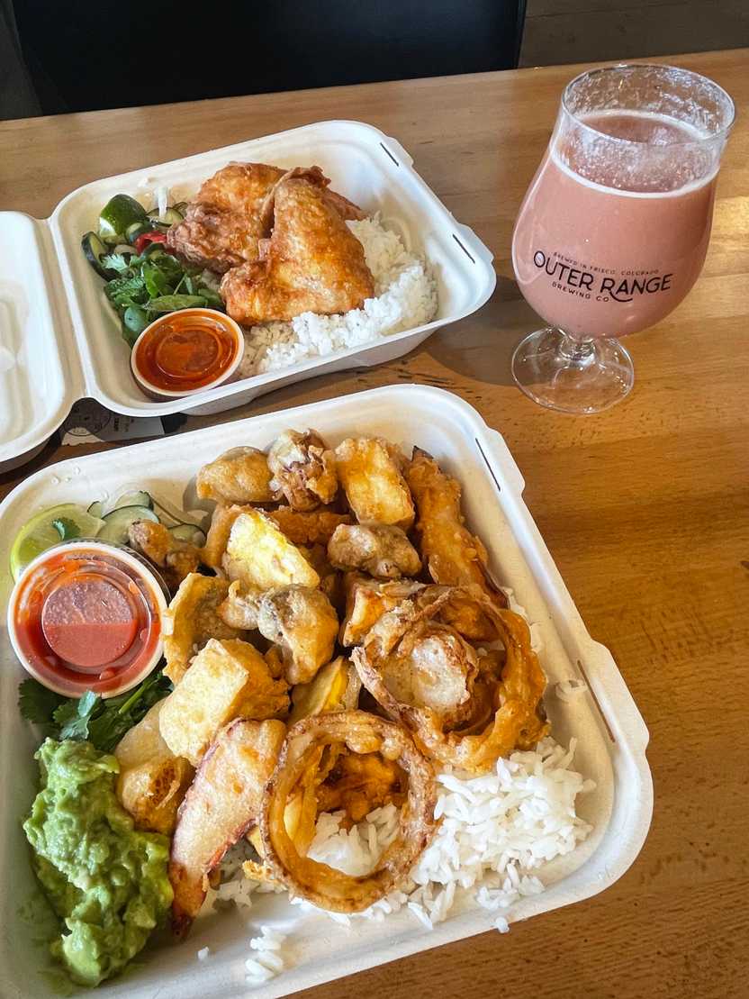 A table with two meals from Bird Craft and a smoothie sour beer. The closest meal is the tofu and veggie bowl, which includes white rice, fried vegtables, tofu, guacamole and a red sauce in a cup. A table with two meals from Bird Craft and a smoothie sour beer. The closest meal is the tofu and veggie bowl, which includes white rice, fried vegtables, tofu, guacamole and a red sauce in a cup.