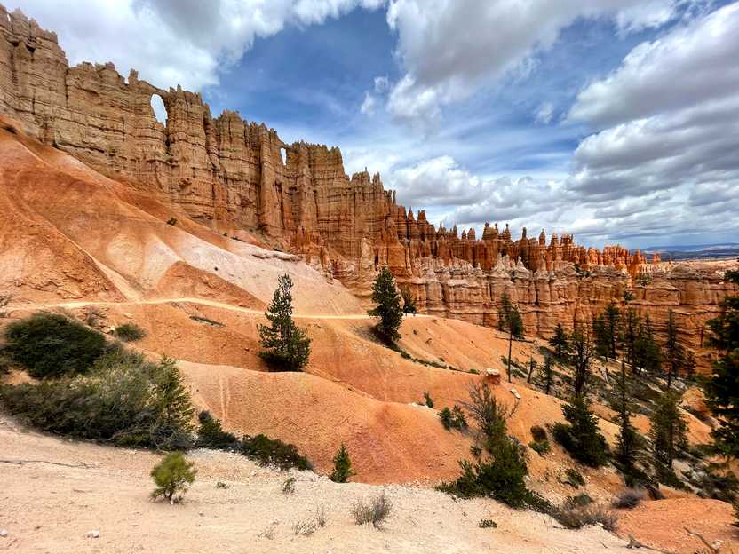 A trail with hoodoo rock formations above and soft hills of orange rocks below.