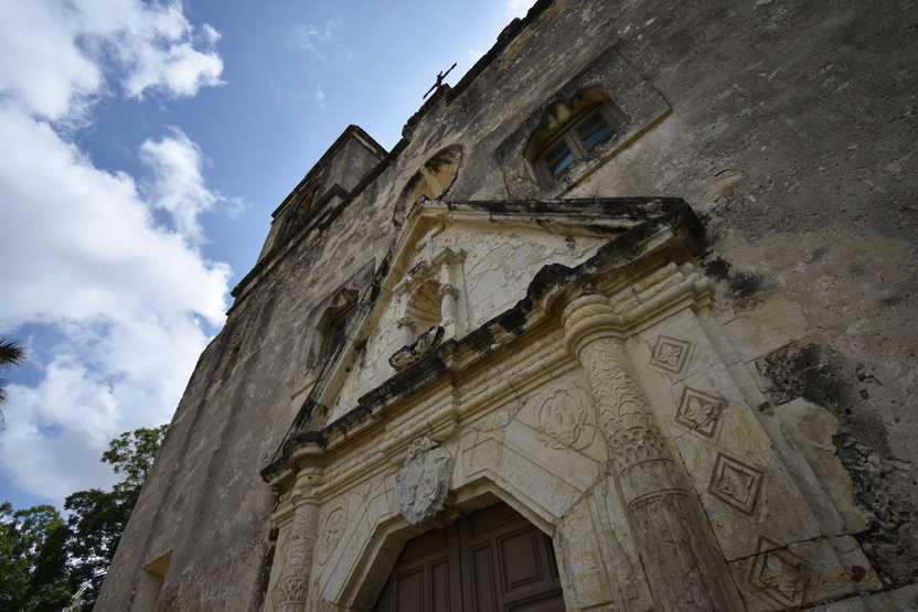 Looking up a Mission Conception. The exterior of the building has some intricate carvings and the building has a lot of discoloration.