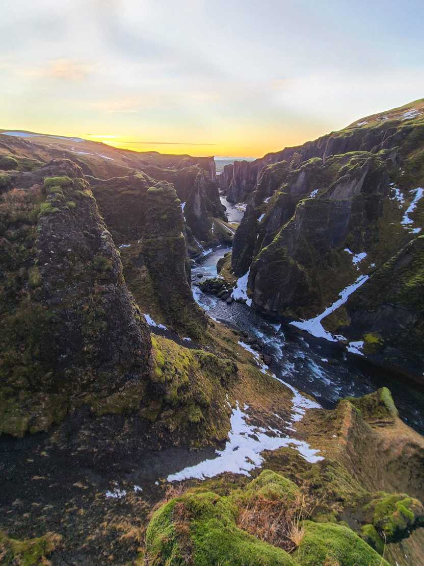 Looking down a rocky, green canyon with a sunrise in the background.