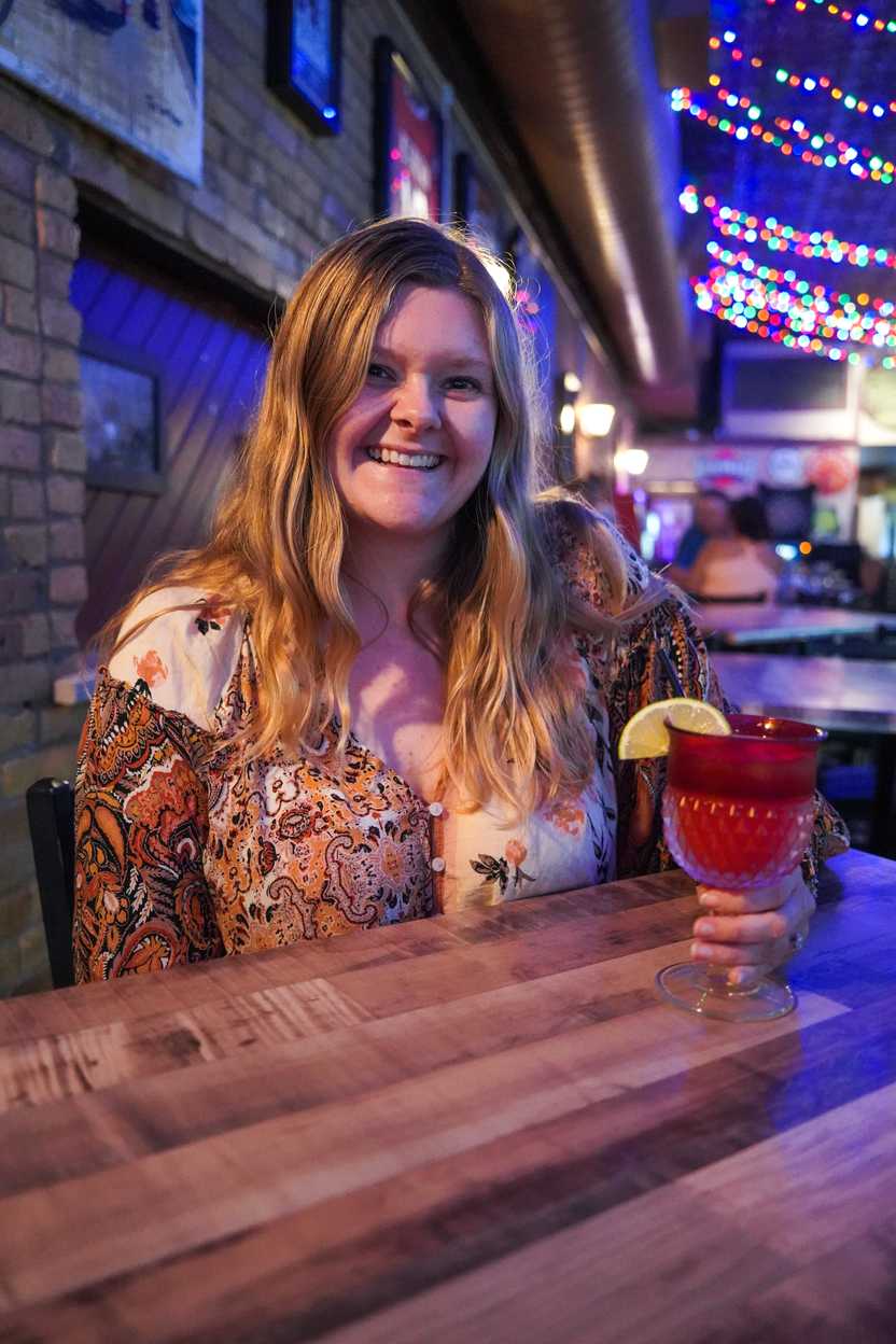 Lydia holding a strawberry margarita cocktail as she sits at a table inside the Pickled Loon Lydia holding a strawberry margarita cocktail as she sits at a table inside the Pickled Loon
