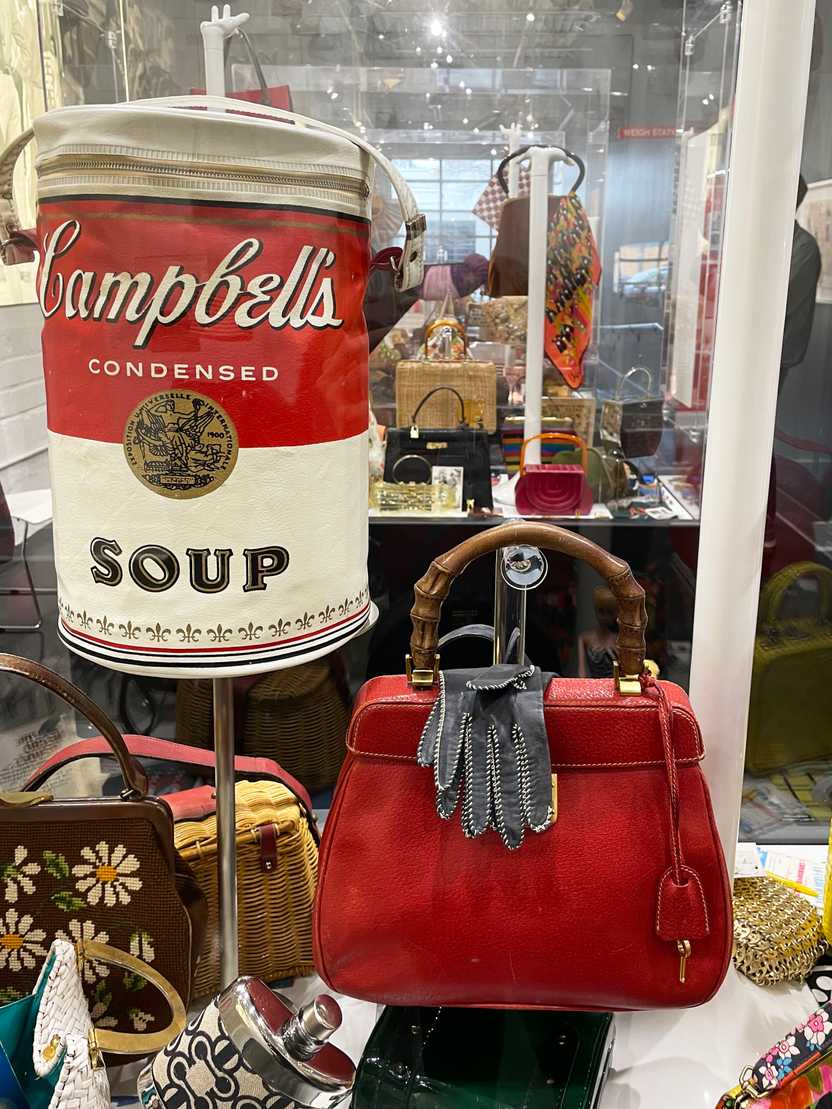 A close up view of a Campbell's soup purse and a red purse with some gloves draped over it. A close up view of a Campbell's soup purse and a red purse with some gloves draped over it.