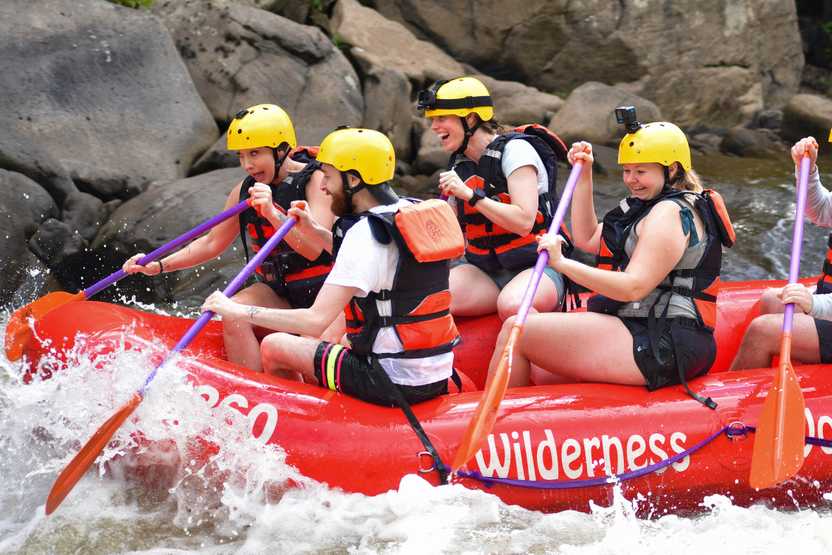 Lydia and 3 others paddling through rapids on the Lower Yough River. Everyone is wearing life vests and helmets.