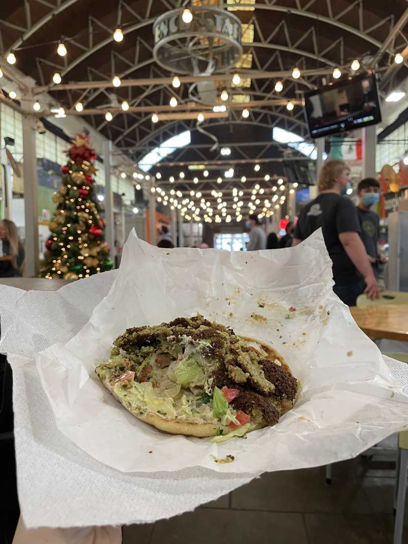 A falafel gyro being held up in the Little Rock Central Market. There is falafel, lettuce and tomato on pita bread. A falafel gyro being held up in the Little Rock Central Market. There is falafel, lettuce and tomato on pita bread.
