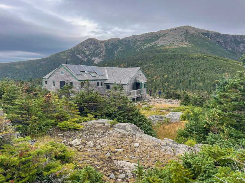 A lodge surrounded by trees with a mountain peak behind it.