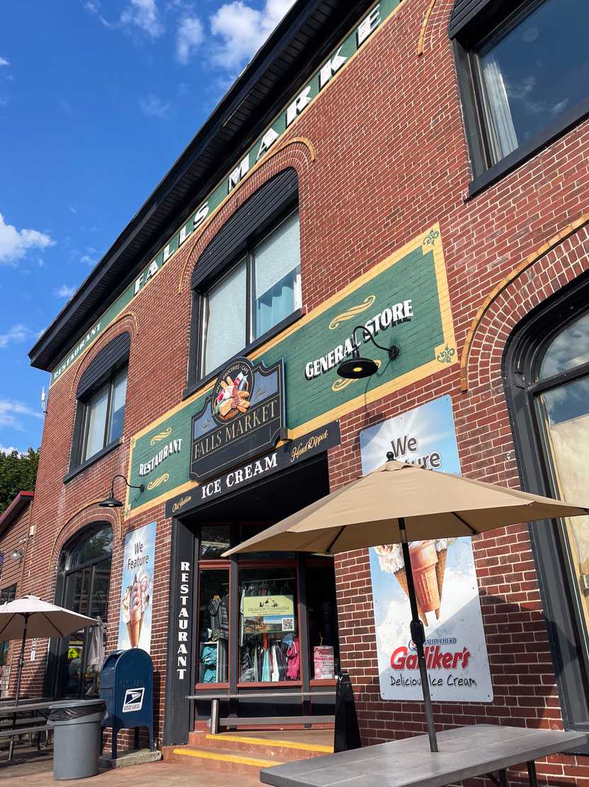 The exterior of Falls Market Restaurant and Inn. It's a brick building with a sign that is painted green and yellow.