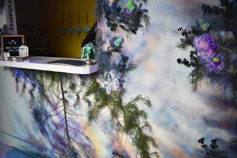 A ticket window next to a wall painted in abtract colors and covered with vines.