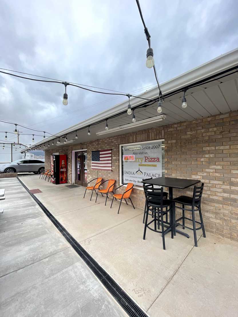 The exterior of Curry Pizza. There are some chairs outside and an American flag.