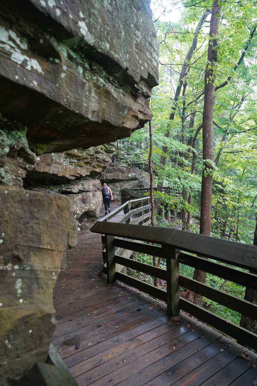 Lydia hiking on a boardwalk trail with a rock overhang on the way to Brandywine Falls.