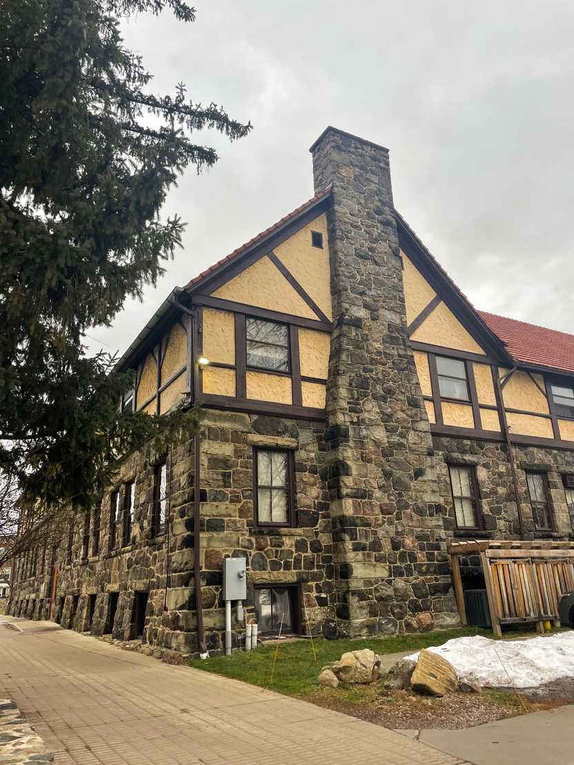 A buiding made of stones that is painted yellow at the top. A large chimney is on the edge of the building.