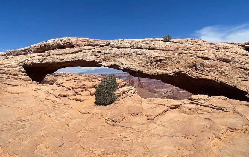 A view looking straight at Mesa Arch in Canyonlands National Park. You can see the some orange formations through the arch.
