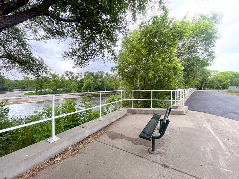 A bench on a sidewalk next to a river along the Beaver Islands Trail