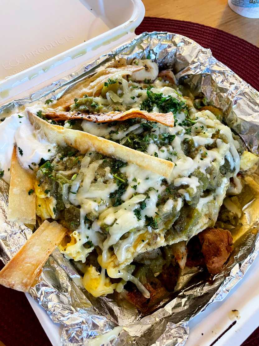 A close up view of huevos rancheros. There are tortilla chips, cheese and green garnish.