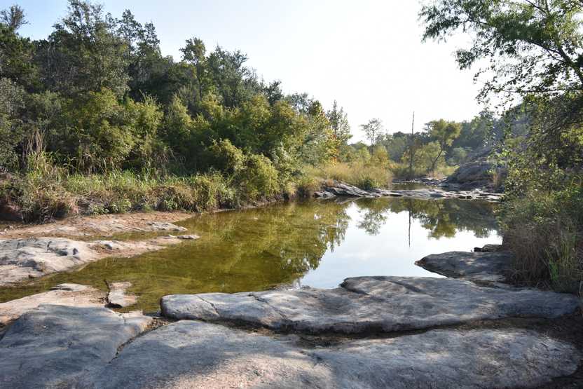 A pond of water next to rocks and trees on teh Valley Spring Creek trail.