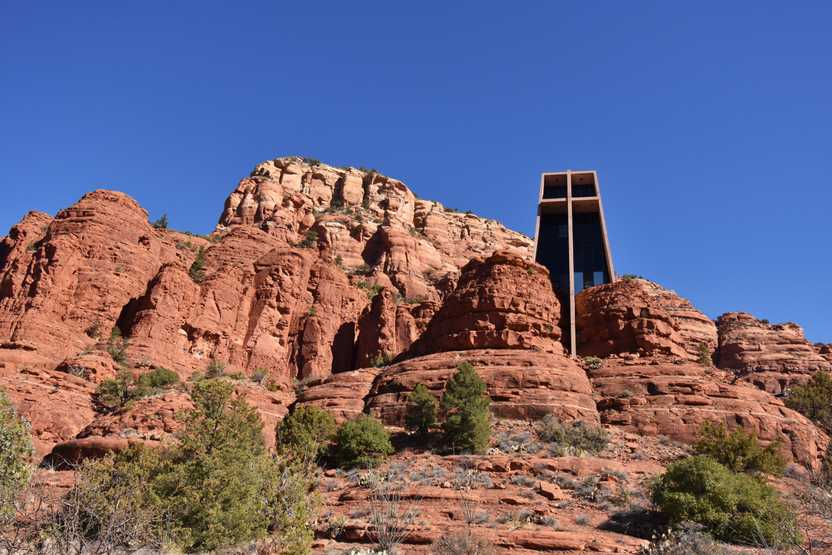 Looking up a glass chapel that rises up from orange rock faces. There are other orange rock faces in the background.