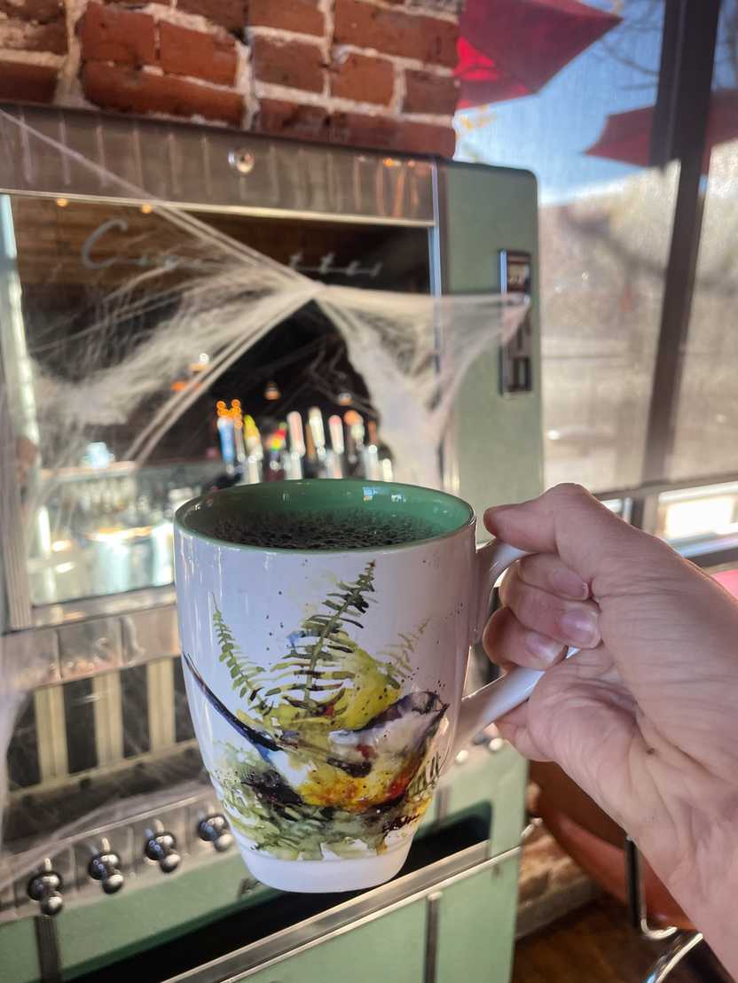 Holding up a mug with a bird on it inside of Denver Biscuit Company.