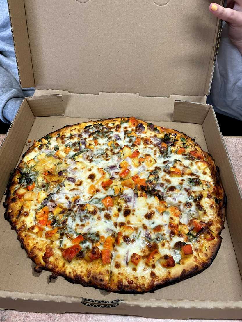 A pizza box with pizza inside. The pizza has cheese and curry chicken.