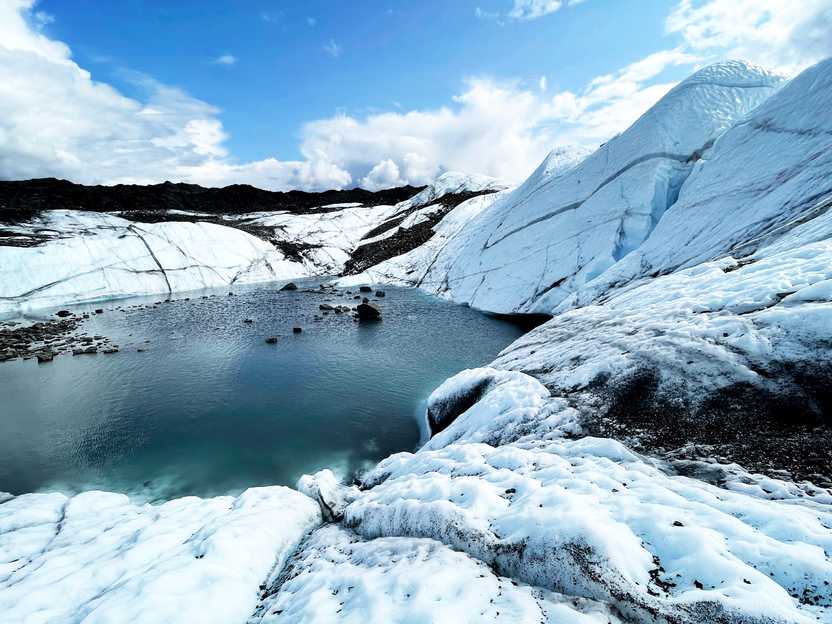 A view looking down at Matanuska Glacier. There is a pool of water surrounded by ice.