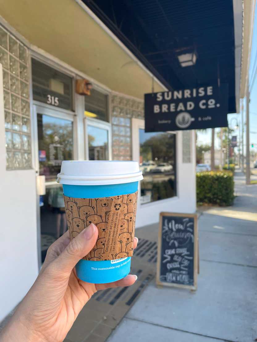 Holding up a blue, paper coffee mug in front of Sunrise Bread Co. Holding up a blue, paper coffee mug in front of Sunrise Bread Co.