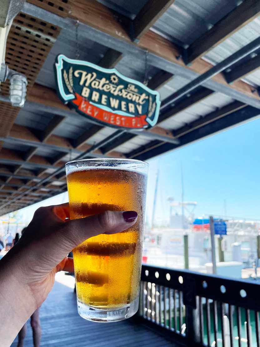 A golden colored beer being held up with a 'Waterfront Brewery' sign in the background
