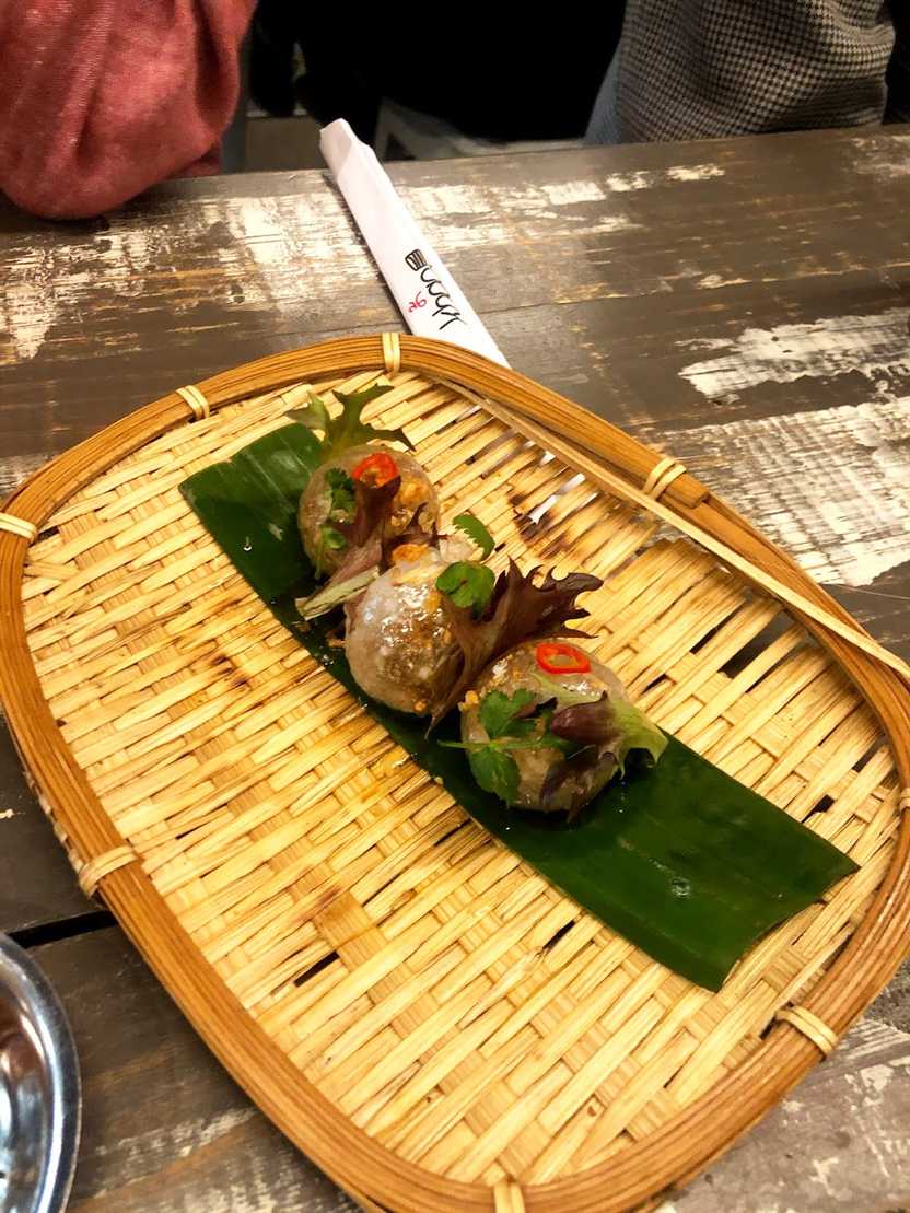 Three dumplings on a woven plate. They are garnished with greens and a small pepper.