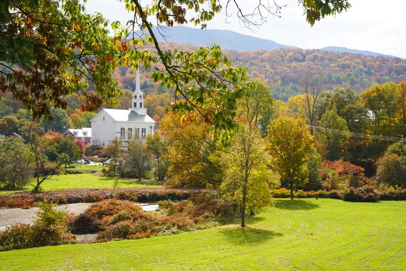 A white church with mountains in the background and trees in the foreground.