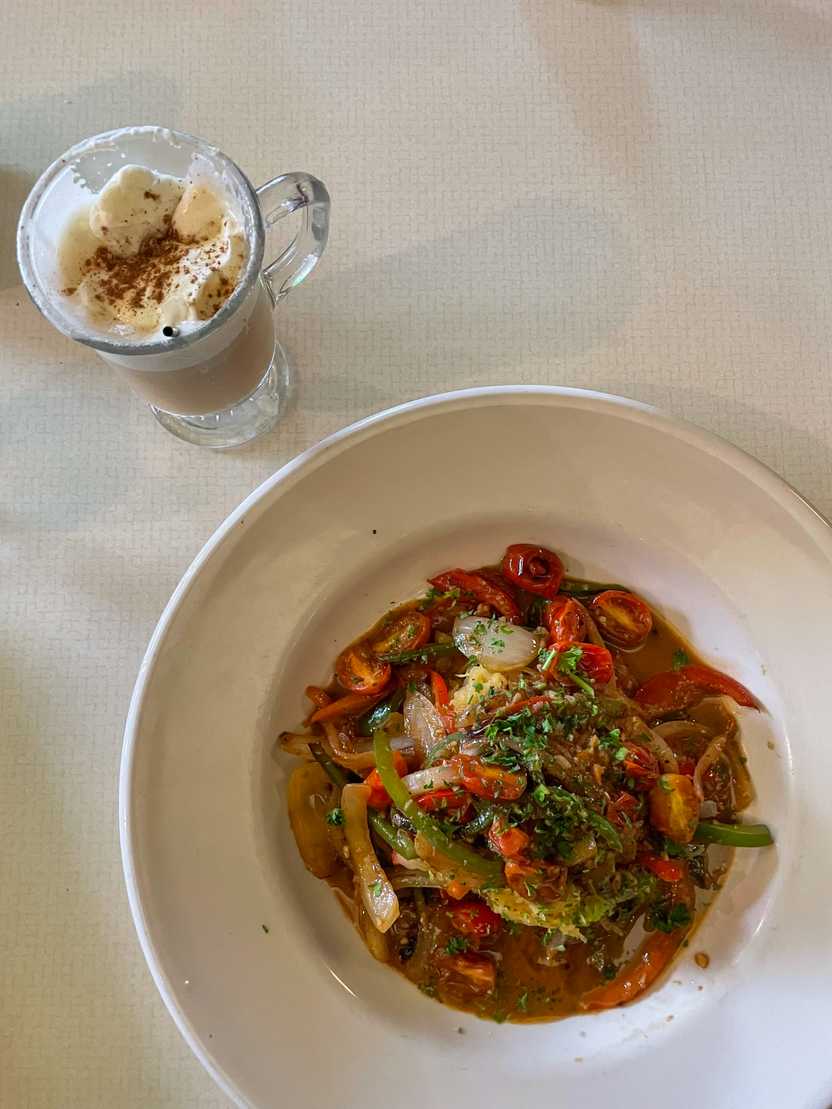 A plate of vegtables covered in sauce next to a cocktail glass with a winter cocktail.