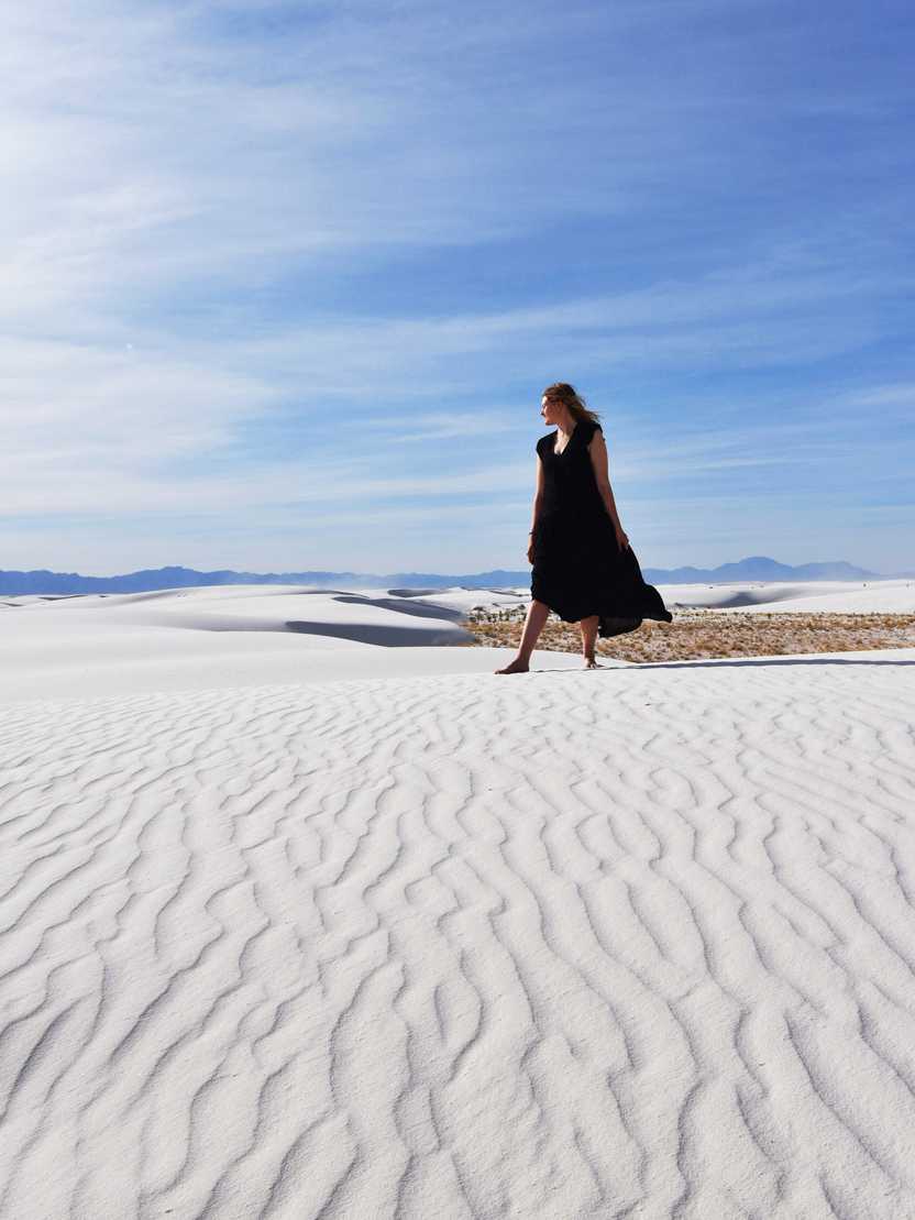 Lydia standing on a sand dune in White Sands wearing a black dress.