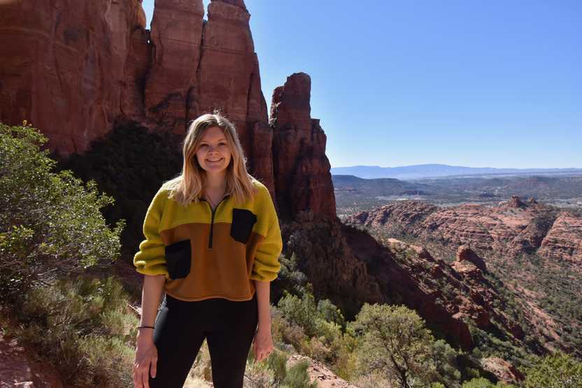 Lydia standing at the viewpoint on the Cathedral Rock trail. She is wearing a yellow  and orange color block sweathshirt.