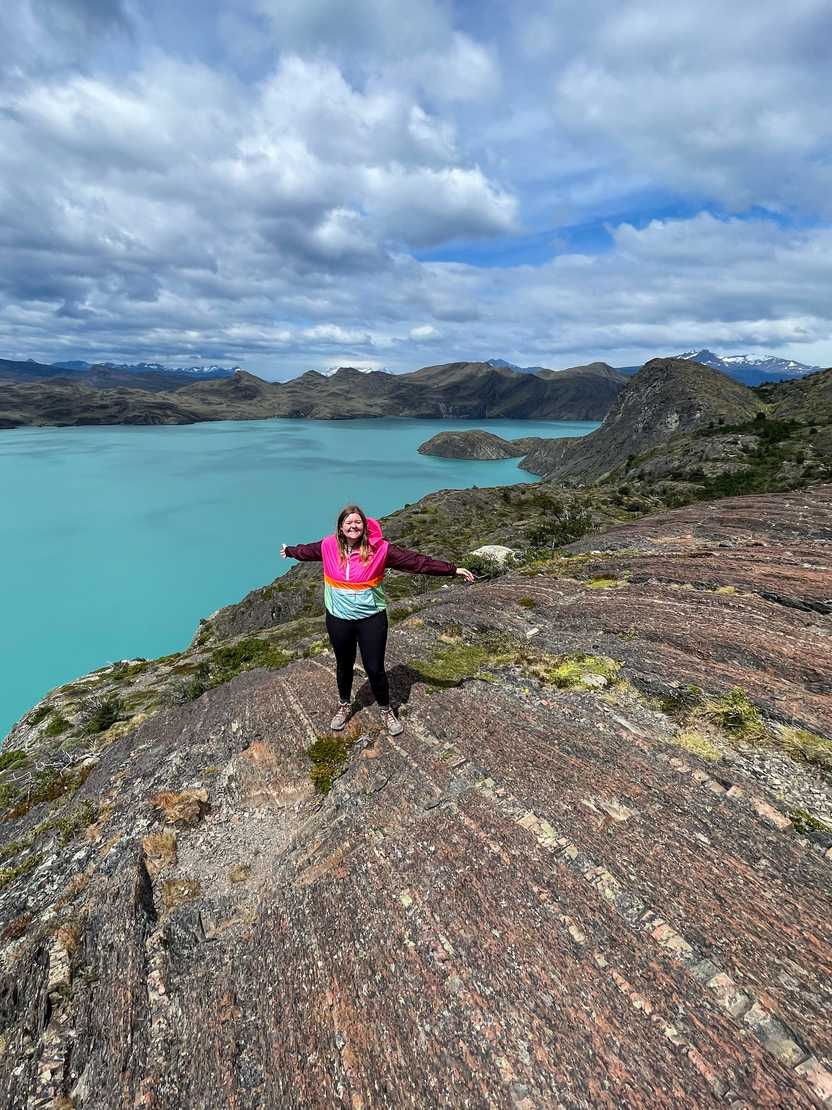 Lydia on a rockface with a bright, blue lake in the background during day w of the W trek.
