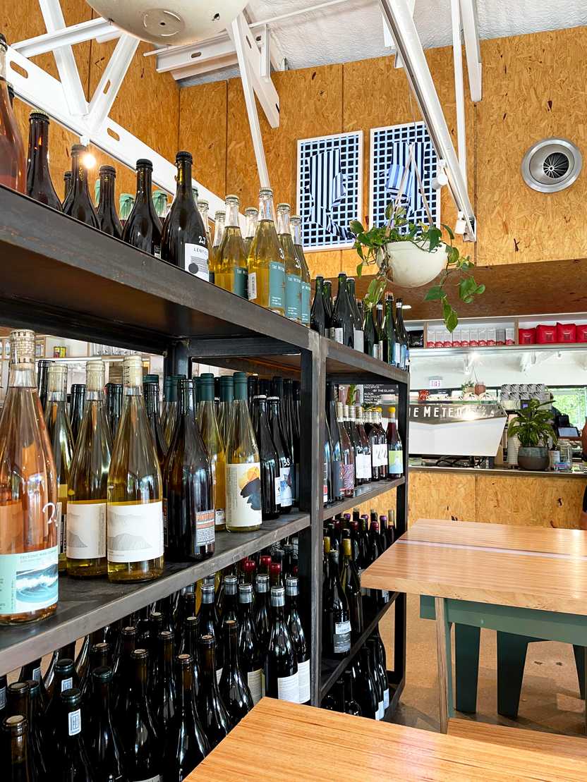 A shelf full of wine bottles next to some wooden tables inside The Meteor.