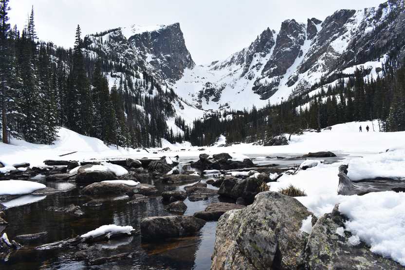 A view of Emerald Lake. There are several rocks in the water and much of the lake is frozen over. There are mountain peaks on the opposite side of the lake.