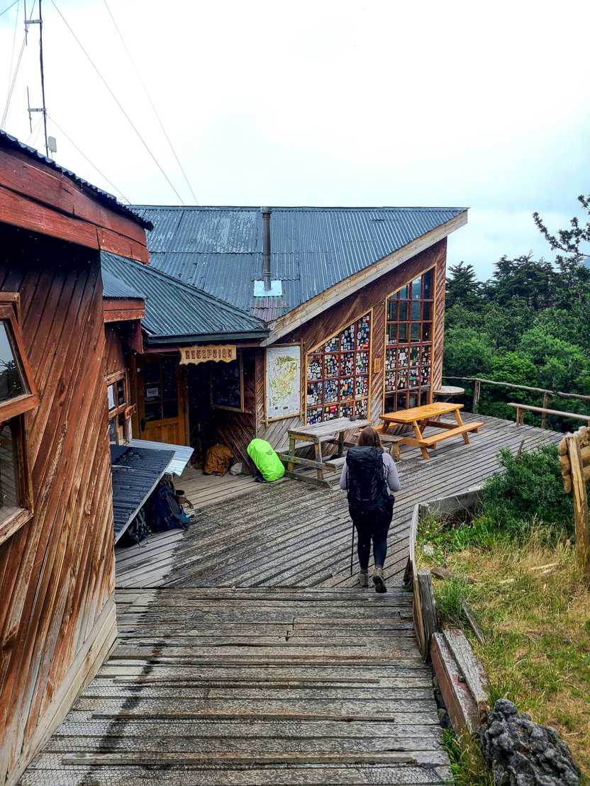 Lydia hiking up the entrance of Los Cuernos. The building is wooden with an angled roof and has stickers on the window.