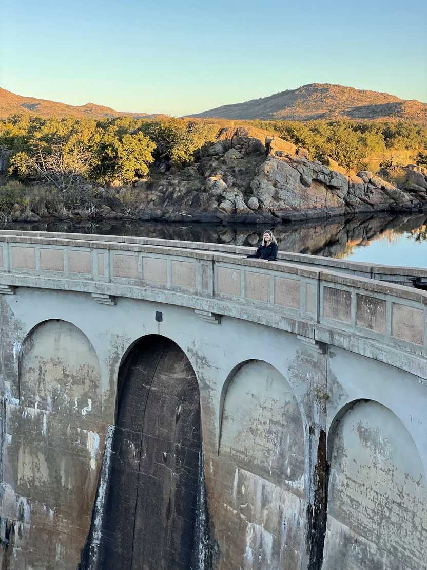 Lydia standing on the Quan Parker Dam. Morning light shines on the mountains in the backgrouhnd.