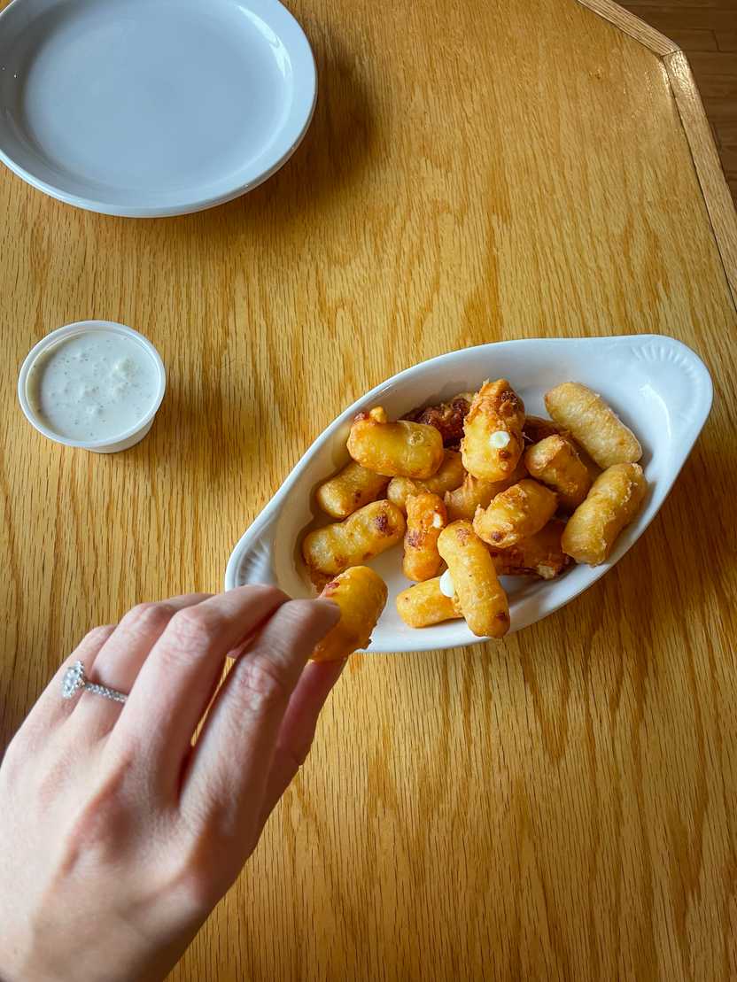 Looking down at a hand picking up a fried cheese curd from a dish in the Grumpy Troll Brew Pub