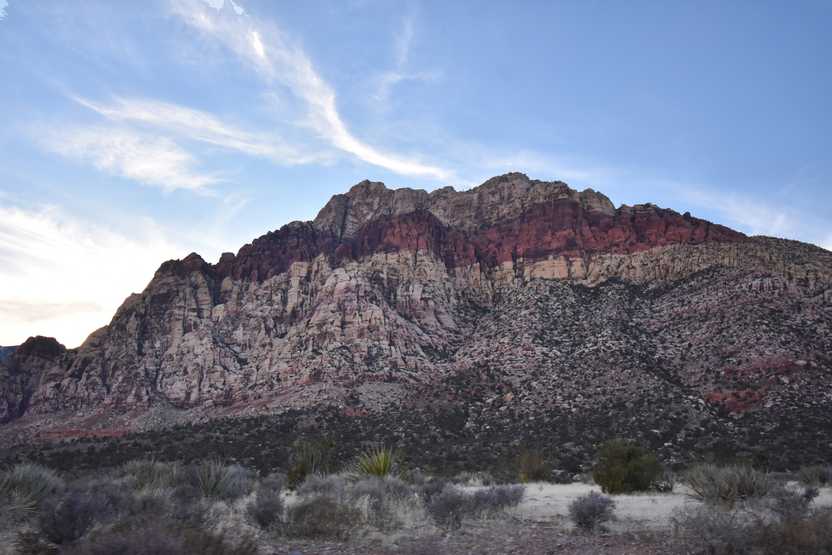 A canyon wall striped with varying colors of red rocks.