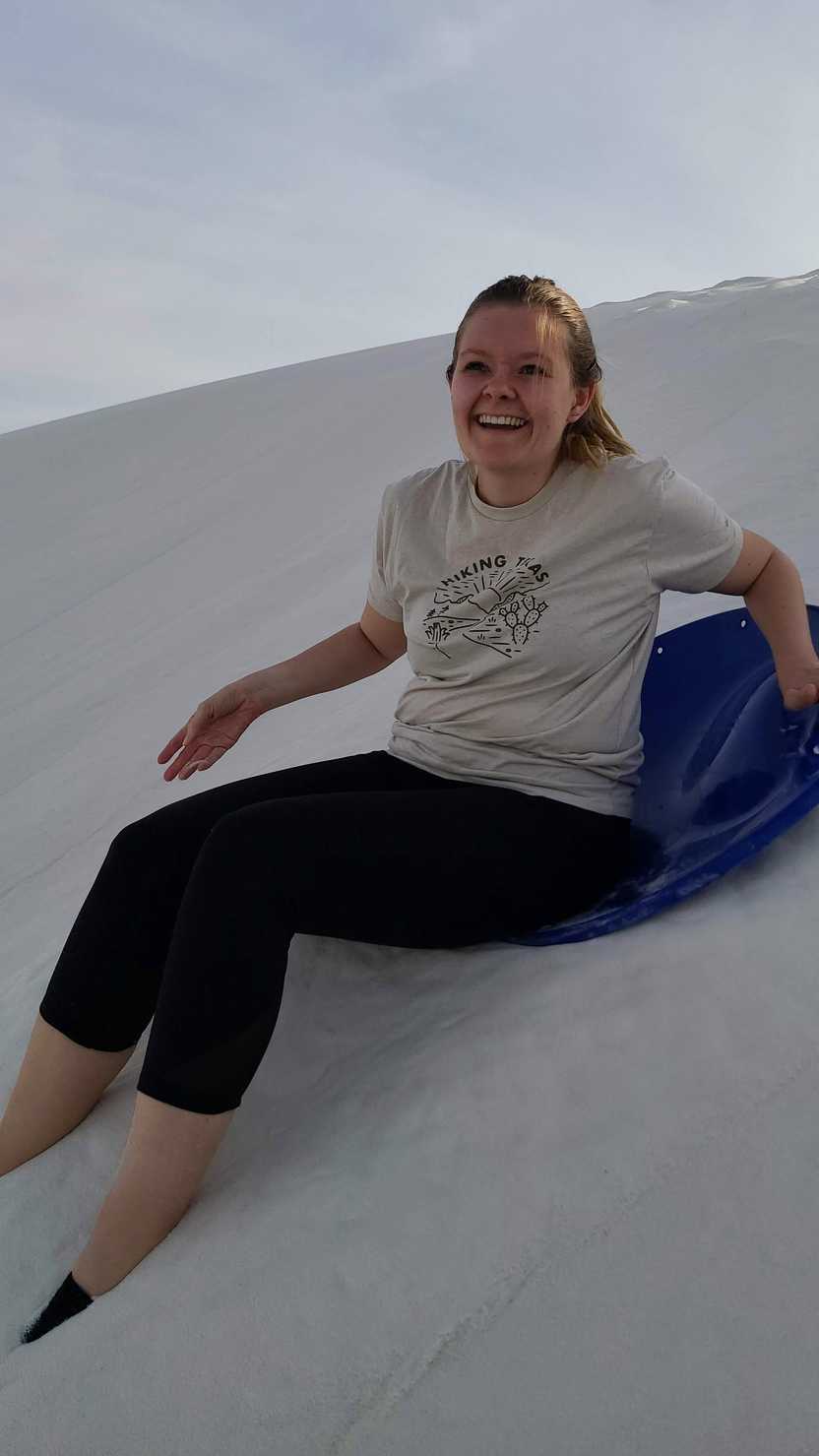 A close up of Lydia having fallen off a sled in White Sands. Her foot is buried in sand.