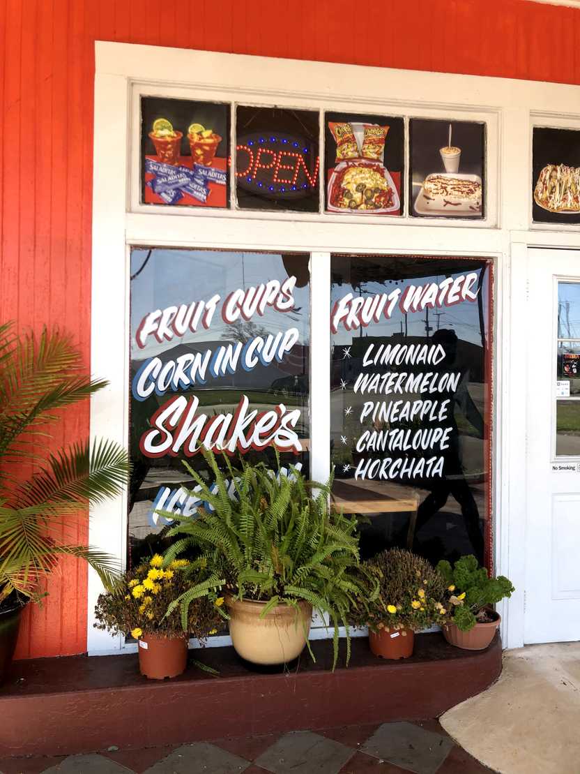 A red building with a white window frame. On the windows, there are lists of some of the offerings, such as "corn in cup," "shakes," "fruit water"
