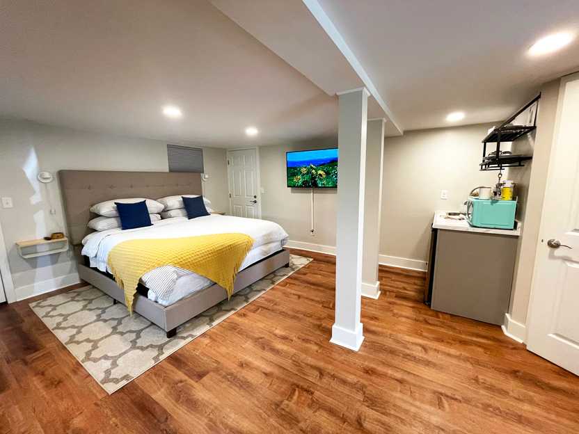 A look inside of a studio apartment Airbnb. There is a large bed with a white blanket and yellow blanket, a wood floor and a blue microwave.